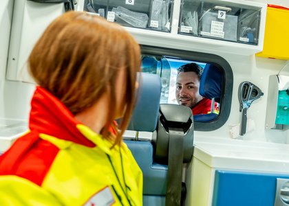 eine junge Frau steht in Uniform vor einem Auto und spricht durch das Beifahrerfenster mit einem Kollegen, der im Auto sitzt