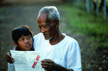 Ein älterer asiatischer Mann und ein junges Mädchen lesen gemeinsam Rotkreuz-Nachrichten. Der Mann umarmt das Kind dabei.