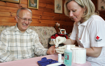 Krankenschwester misst im Rahmen der mobilen Pflege den Blutzucker eines Patienten.