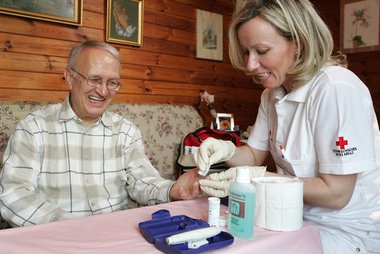 Krankenschwester misst im Rahmen der mobilen Pflege den Blutzucker eines Patienten.