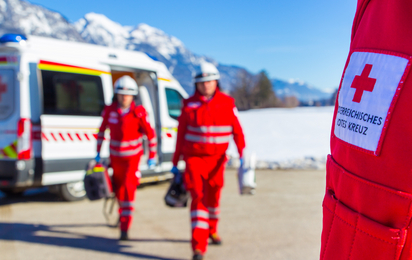 Zwei Sanitäter mit Gerätschaften gehen vom RTW Richtung eines weiteren Sanitäters, dessen Rotes Kreuz zu sehen ist.