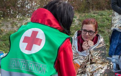 Eine Mitarbeiterin der Krisenintervention spricht mit einer Frau, die in einer Rettungsdecke eingewickelt ist. Sie bekommt psychosoziale Unterstützung während einer Krise