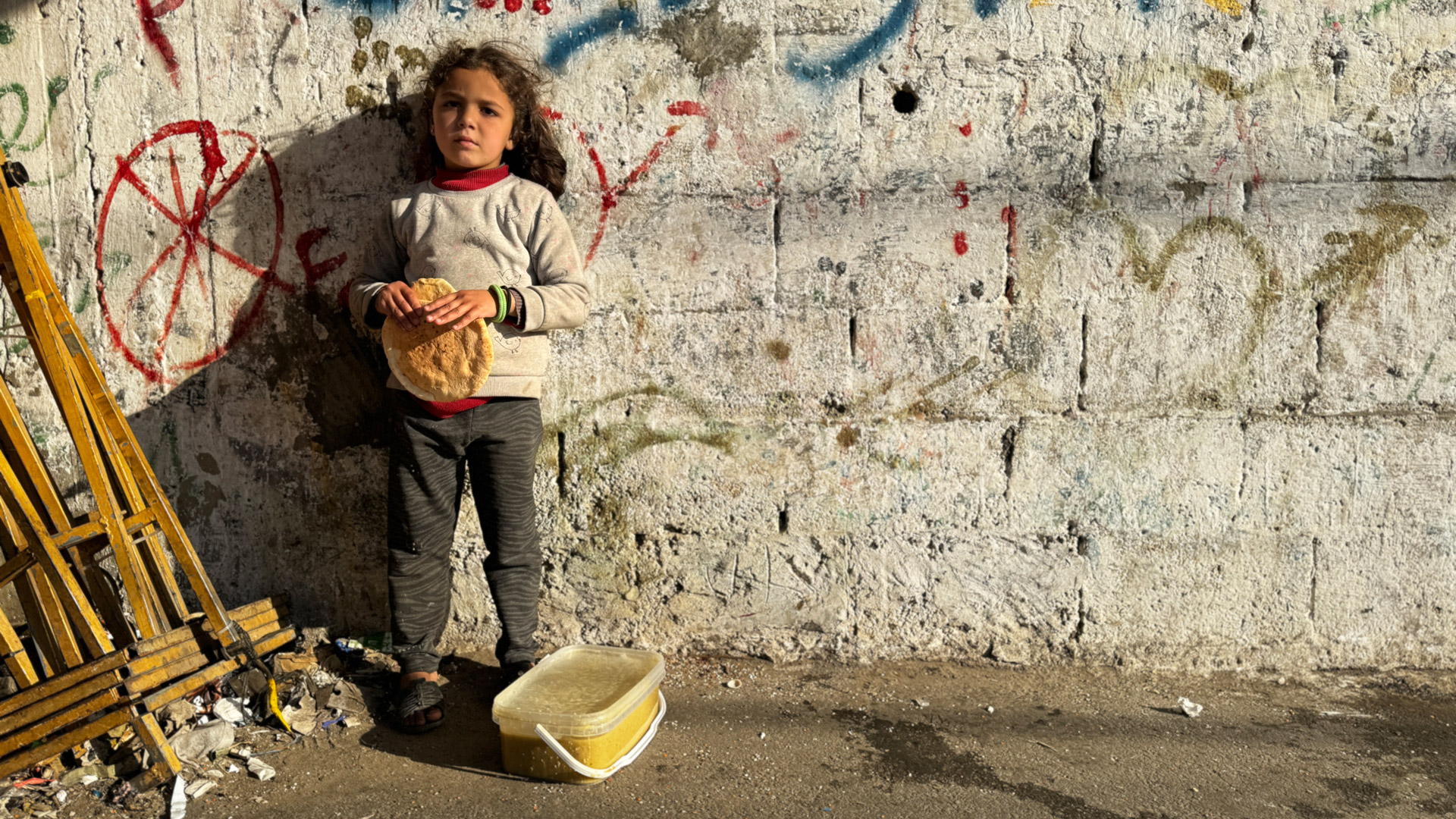 Mädchen in Gaza steht an einer Wand und hält Brot in der Hand