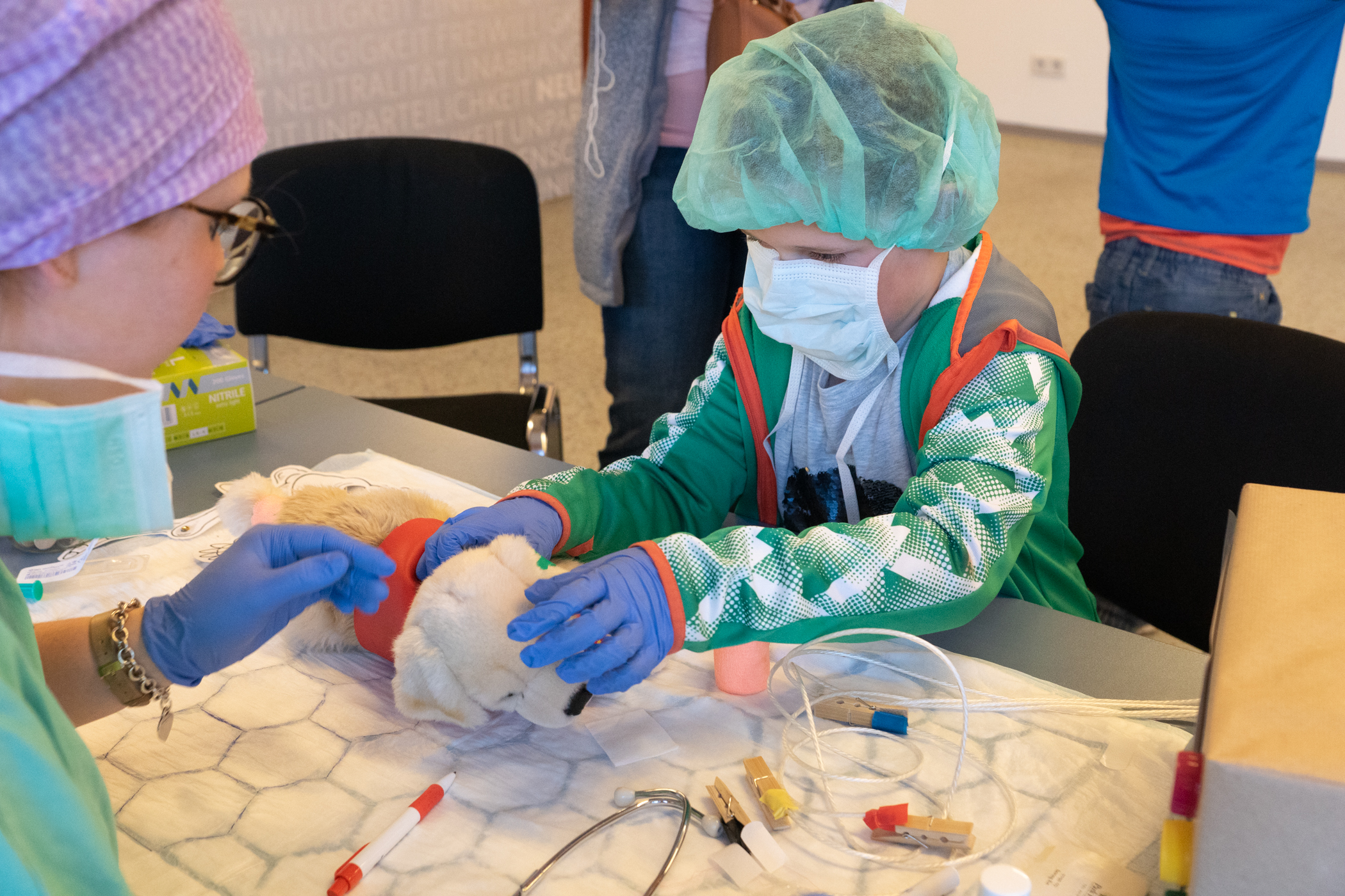 Ein Kind in OP-Kleidung untersucht sein Stofftier im Rahmen der Teddyklinik