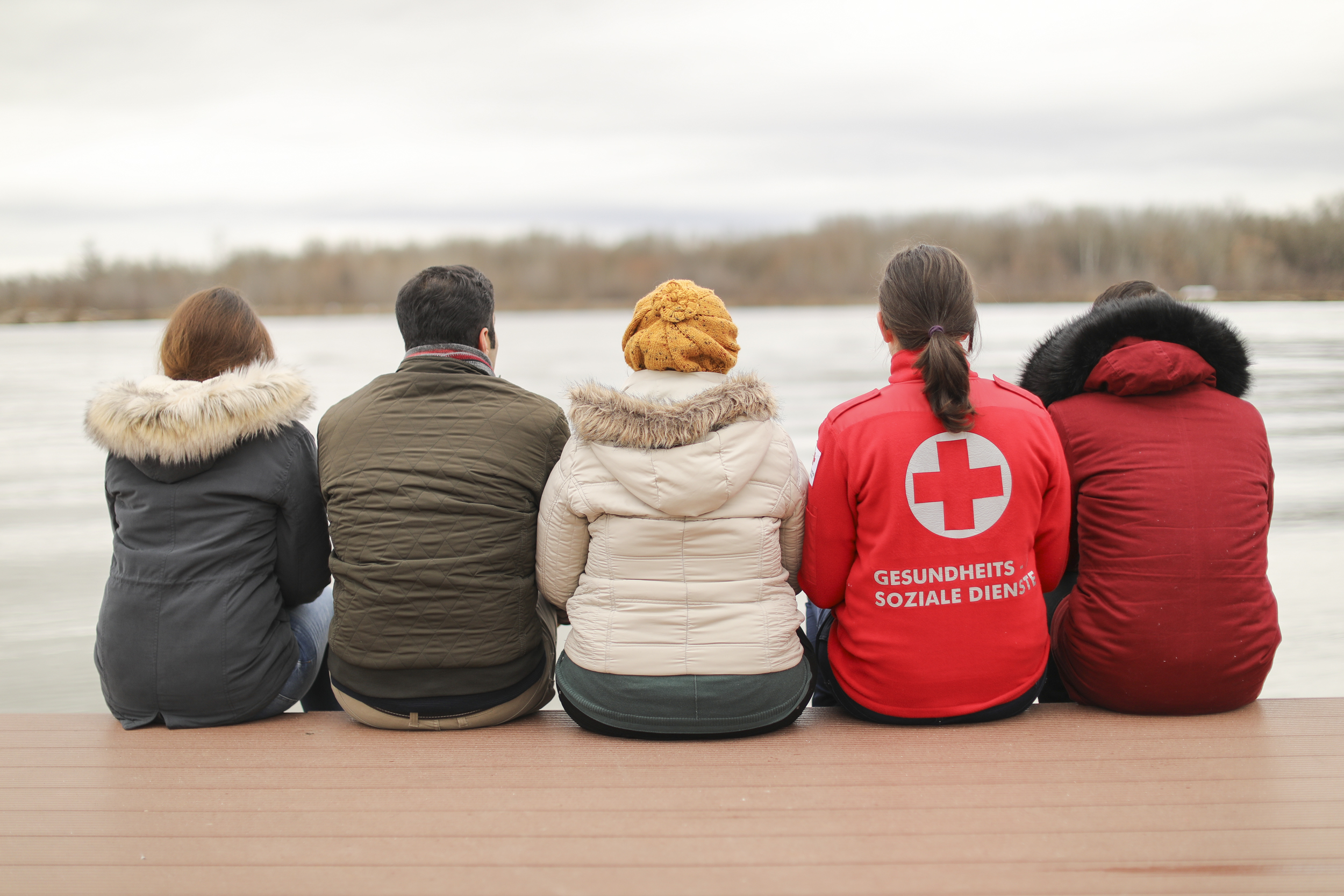 Eine Familie sitzt mit dem Rücken zu uns vor einem See.