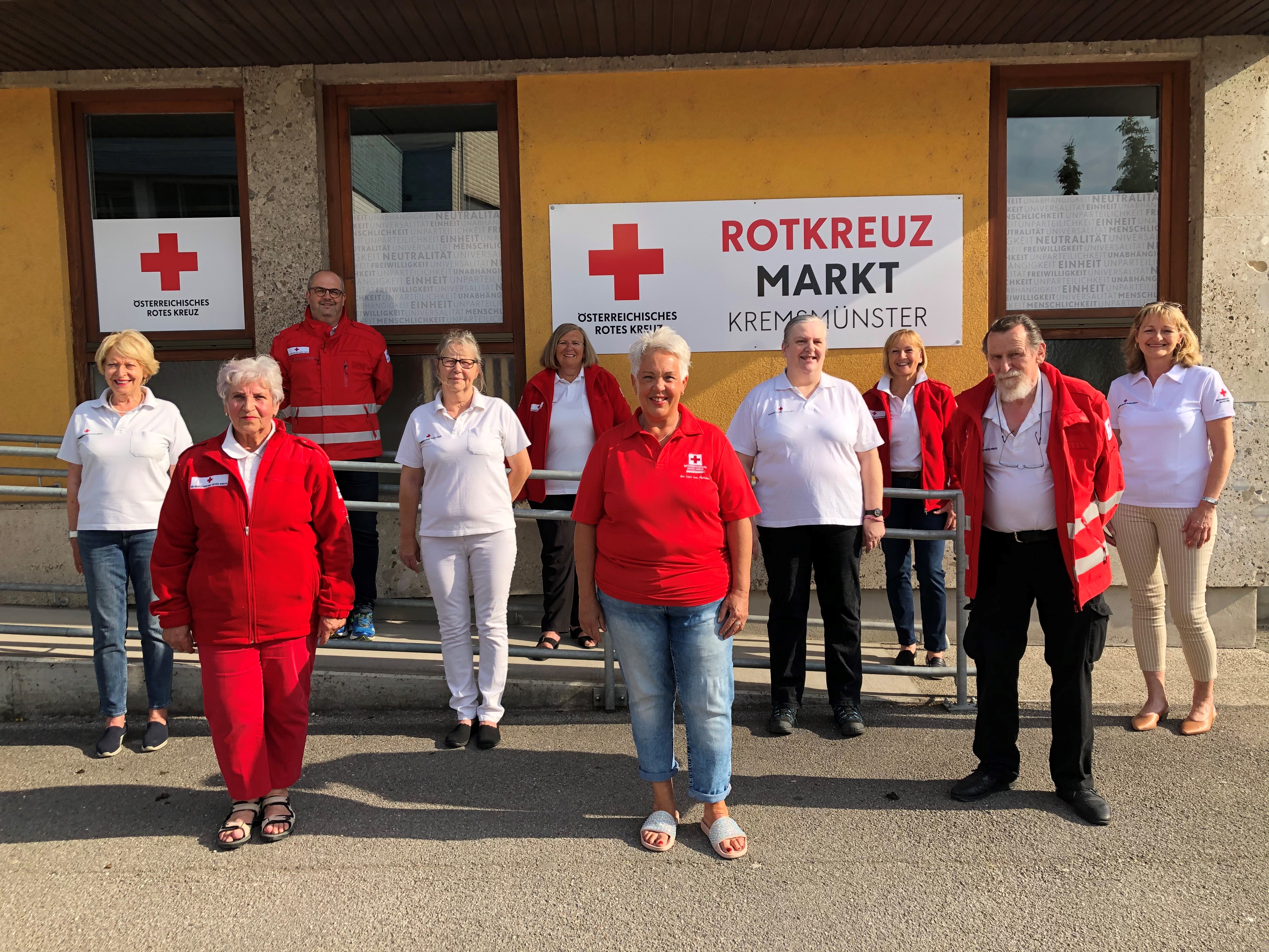 Ein Teil der freiwilligen Mitarbeiterinnen und Mitarbeiter, die von Beginn an im Rotkreuz-Markt mitwirken, stehen in drei Reihen vor dem Rotkreuz-Markt