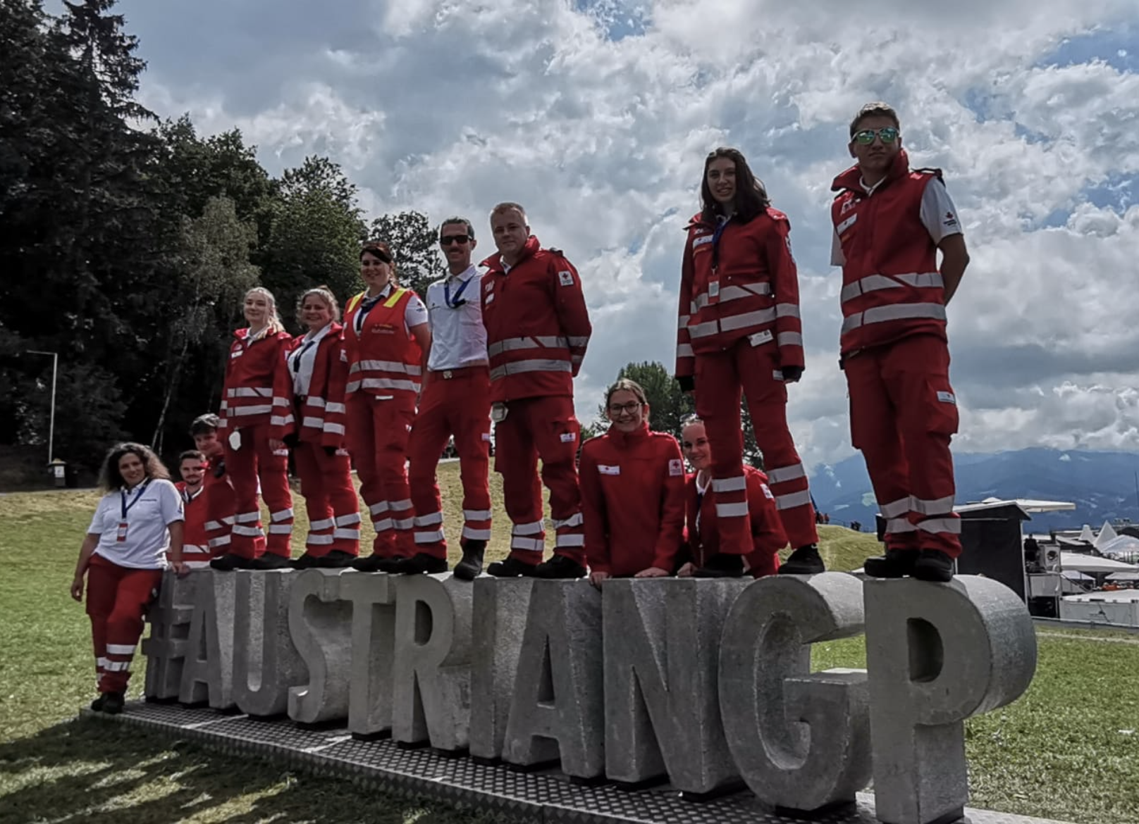 Ein Team an Rotkreuz-Sanitäter:innen steht auf und neben einem #AustrianGP-Schiftzug aus Beton am Formel 1 Grand Prix 2022 in Spielberg.