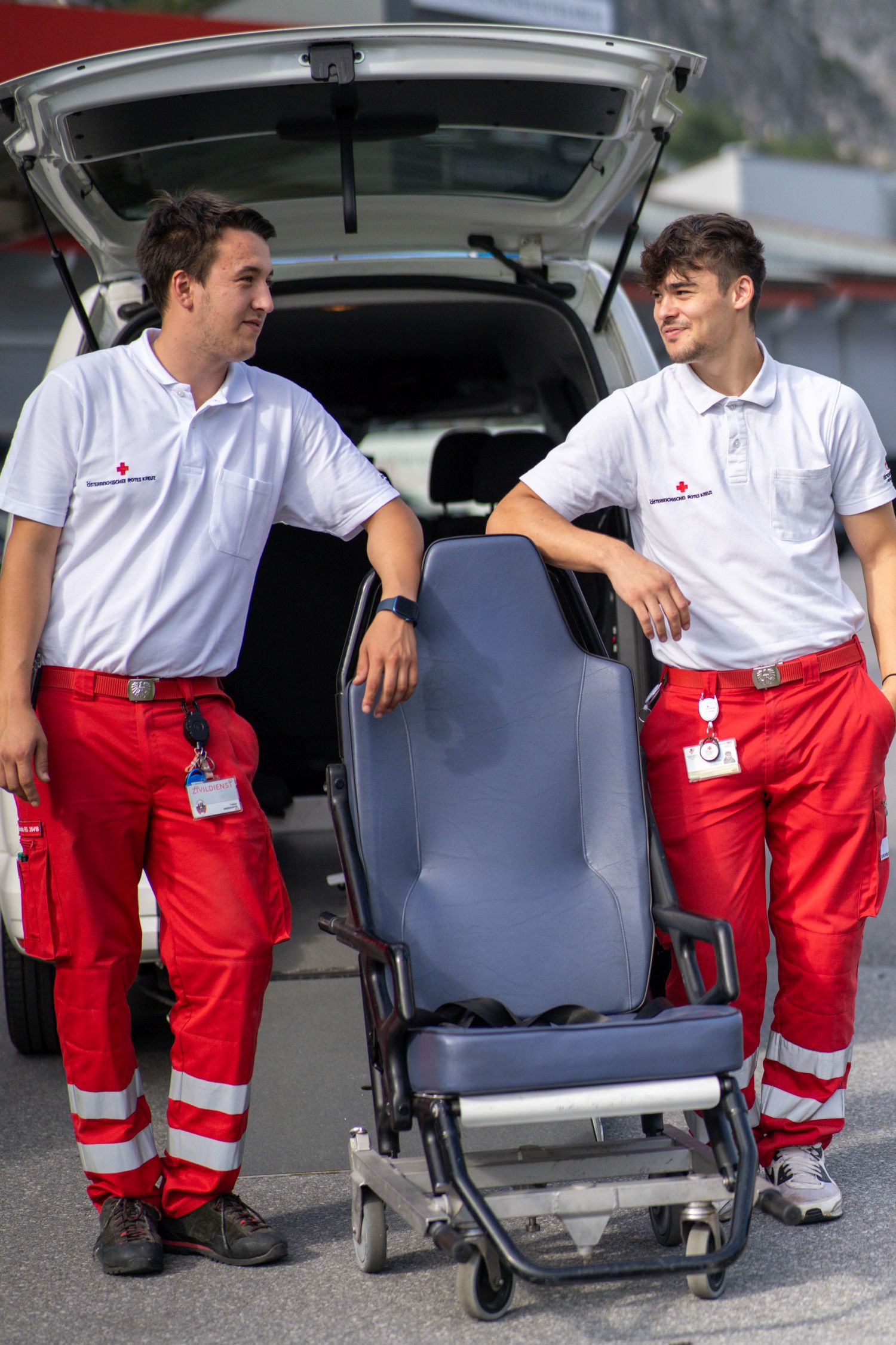 Zwei Zivildiener in Uniform stehen mit einem Tragsessel vor einem Rettungsauto, das hinten geöffnet ist