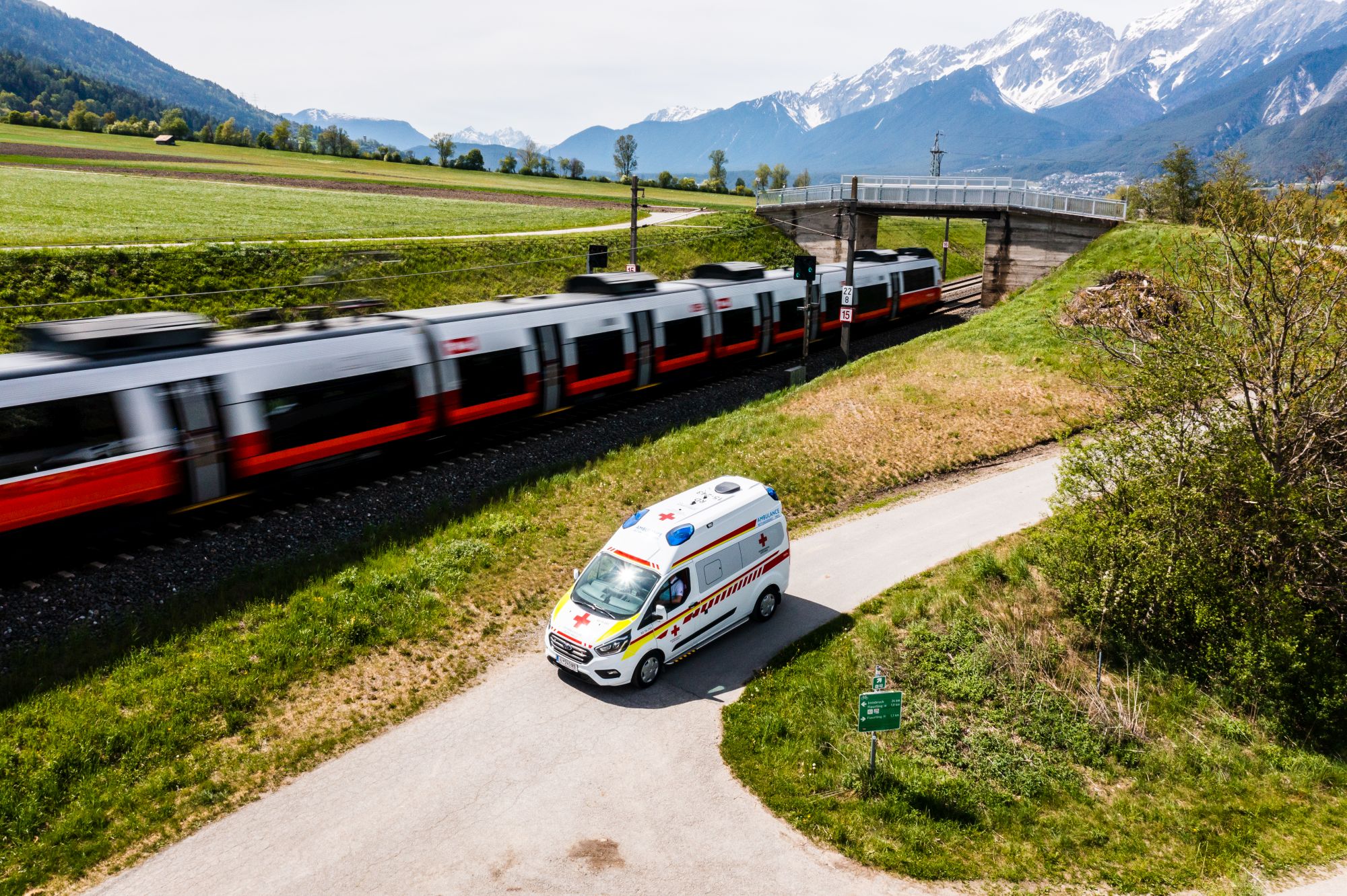 ein von einer Drohe fotografiertes Rettungsfahrzeug fährt neben einem Zug der ÖBB